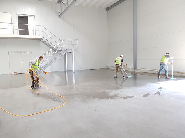 three men in traffic vests cleaning a warehouse floor